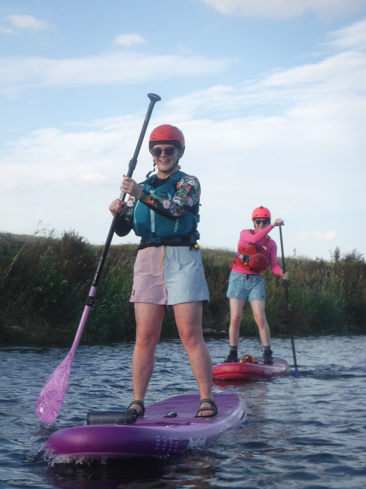 Two paddleboarders wearing buoyancy aids and helmets on calm water